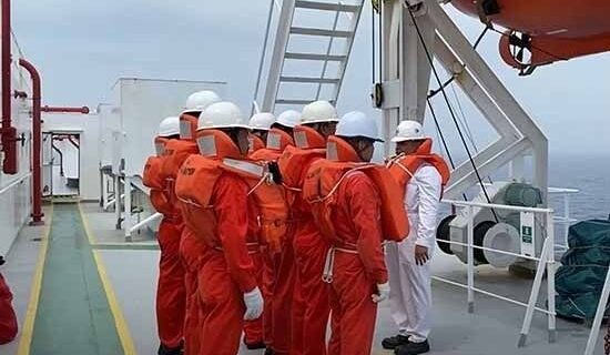 Crewmitglieder in orangefarbenen Schutzanzügen an Bord eines Schiffs