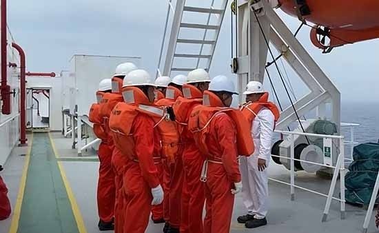 Crewmitglieder in orangefarbenen Schutzanzügen an Bord eines Schiffs