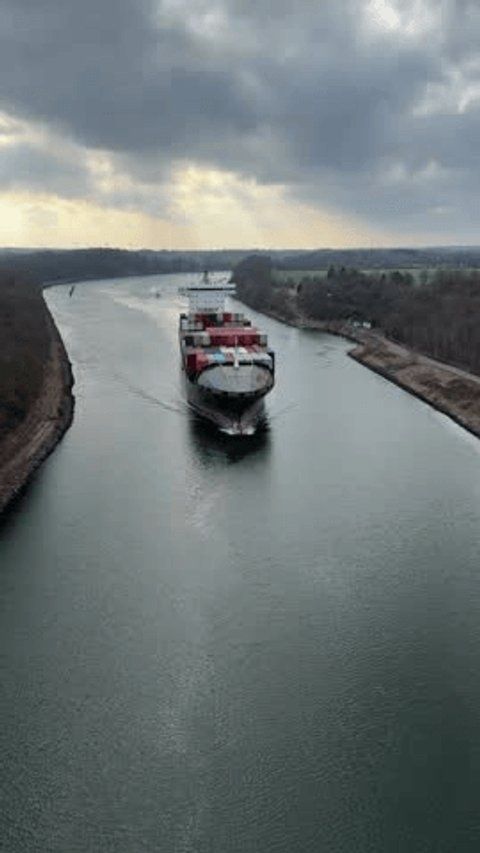 Containerschiff fährt durch einen geradlinigen Kanal unter dunklen Wolken
